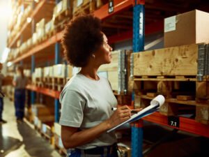 african american worker writing inventory list while checking stock storage room
