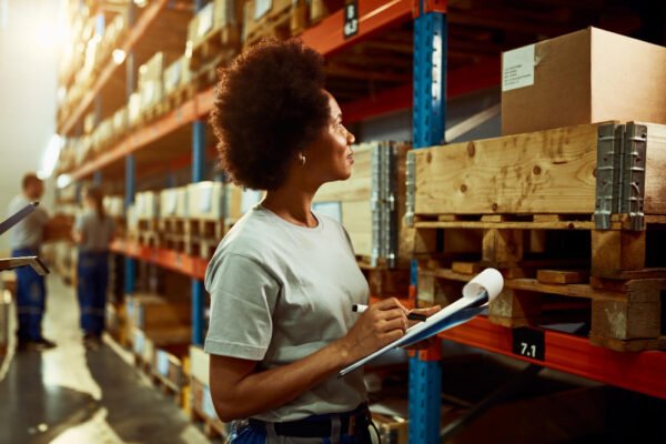 african american worker writing inventory list while checking stock storage room